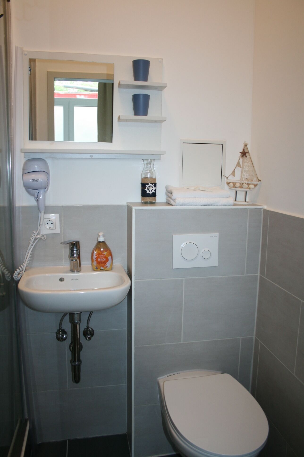 A compact bathroom with a white sink, a handheld hair dryer, a bottle of soap, and a toilet.
