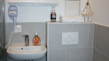 A compact bathroom with a white sink, a handheld hair dryer, a bottle of soap, and a toilet.