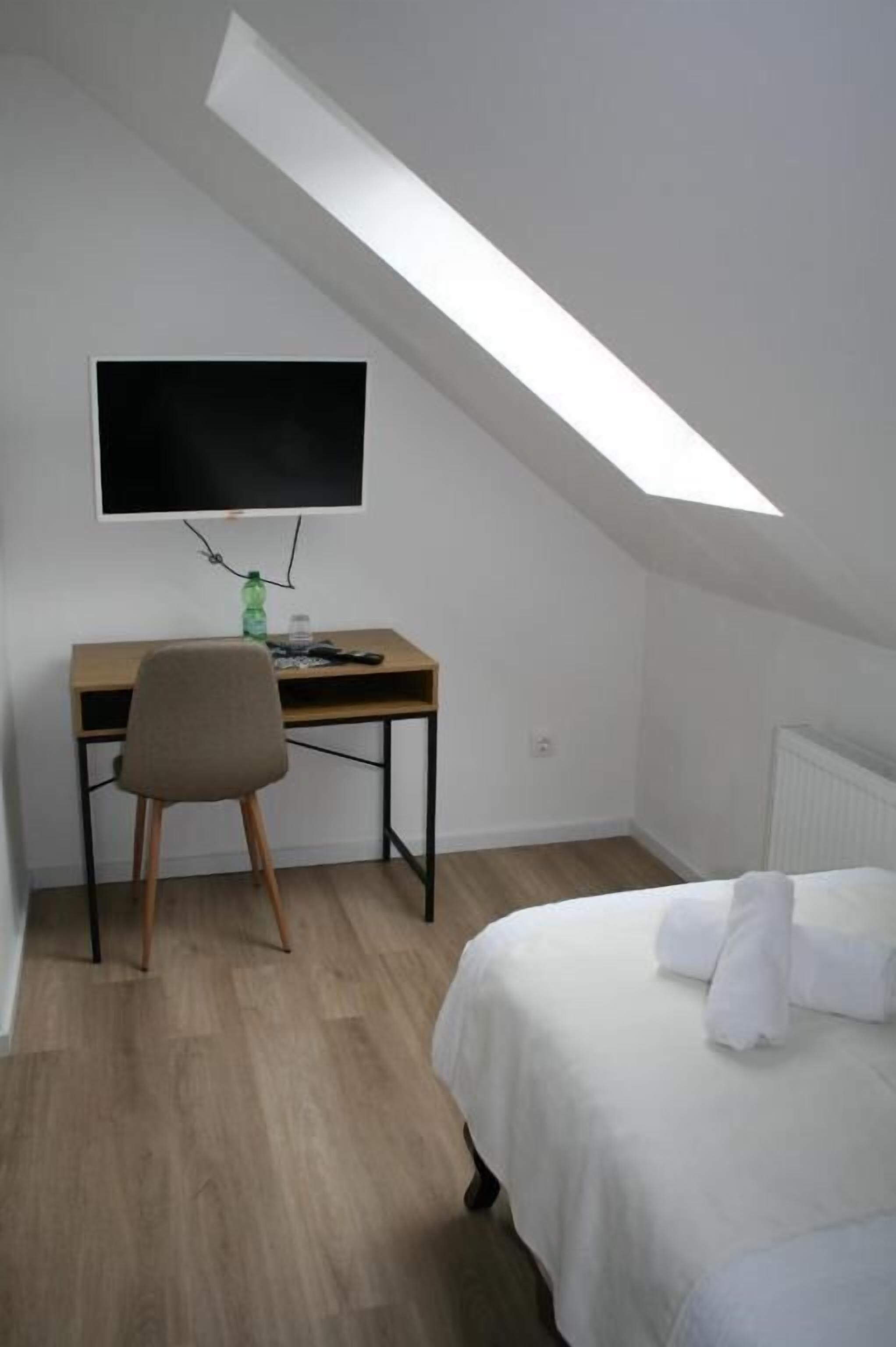 Una habitación con cama, un escritorio con silla, televisión y tragaluz.