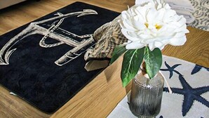 A hotel room with two beds, a small table, a decorative vase with a flower, and a starfish-patterned rug. - Hotel am Seehafen (Hamburg)