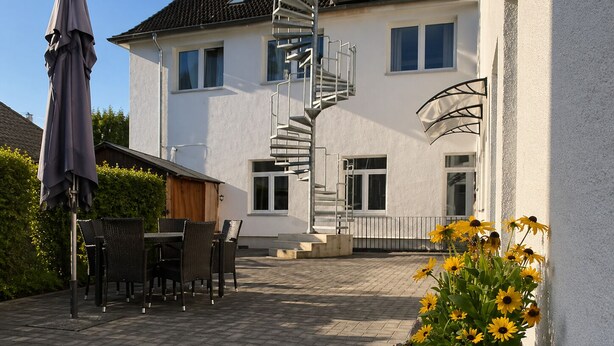 A house with a spiral staircase, a patio with chairs, and a flower bed. - Hotel am Seehafen (Hamburg)