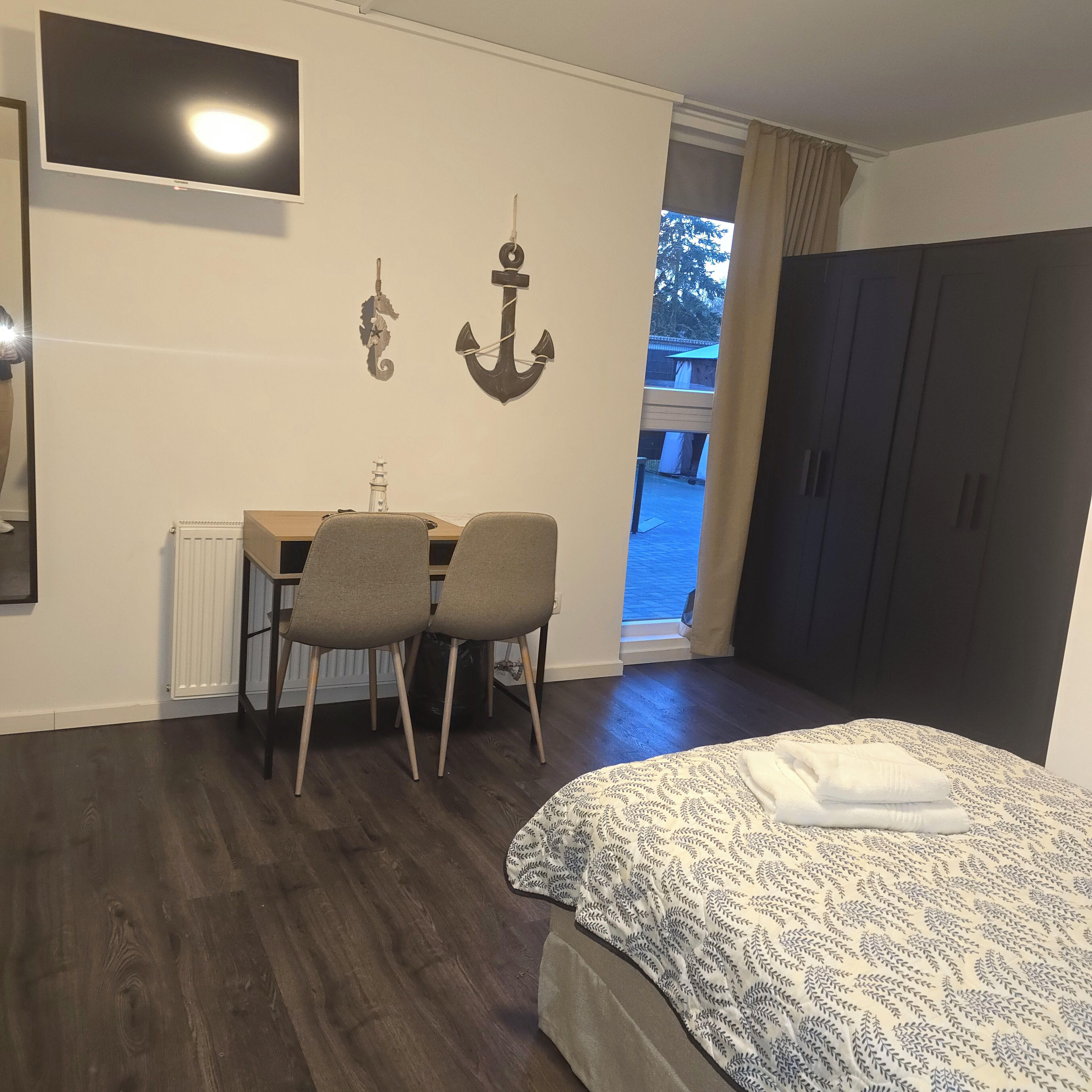 Una habitación con una cama, un escritorio con dos sillas, un televisor y una decoración con forma de ancla.