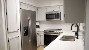 A modern kitchen with white cabinetry, stainless steel appliances including a refrigerator, microwave, and oven, and a large sink. - Family-Friendly Home at the Heart of DFW- close to all popular attrations! (Euless)