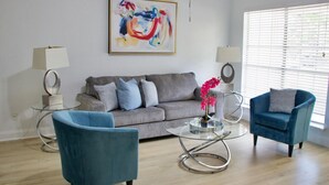 A modern living room with a grey sofa, two blue armchairs, a glass coffee table, and a colorful abstract painting on the wall. - Family-Friendly Home at the Heart of DFW- close to all popular attrations! (Euless)