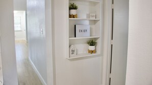 A hallway with white walls and a white door. There are three shelves with decorative items and a sign that says "ENJOY". - Family-Friendly Home at the Heart of DFW- close to all popular attrations! (Euless)