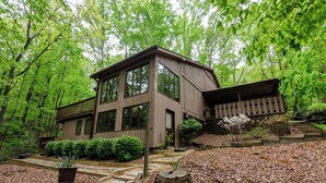 A wooden cabin with large windows, surrounded by a forest. - Cozy and serene fishing cabin, Family Traditions,  private dock and lake views. (Gainesville)