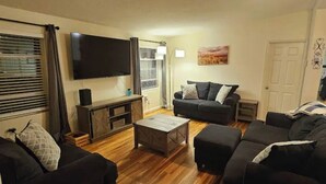 Ein Wohnzimmer mit einem Flachbildfernseher, zwei Sofas, einem Couchtisch und einer Tür.