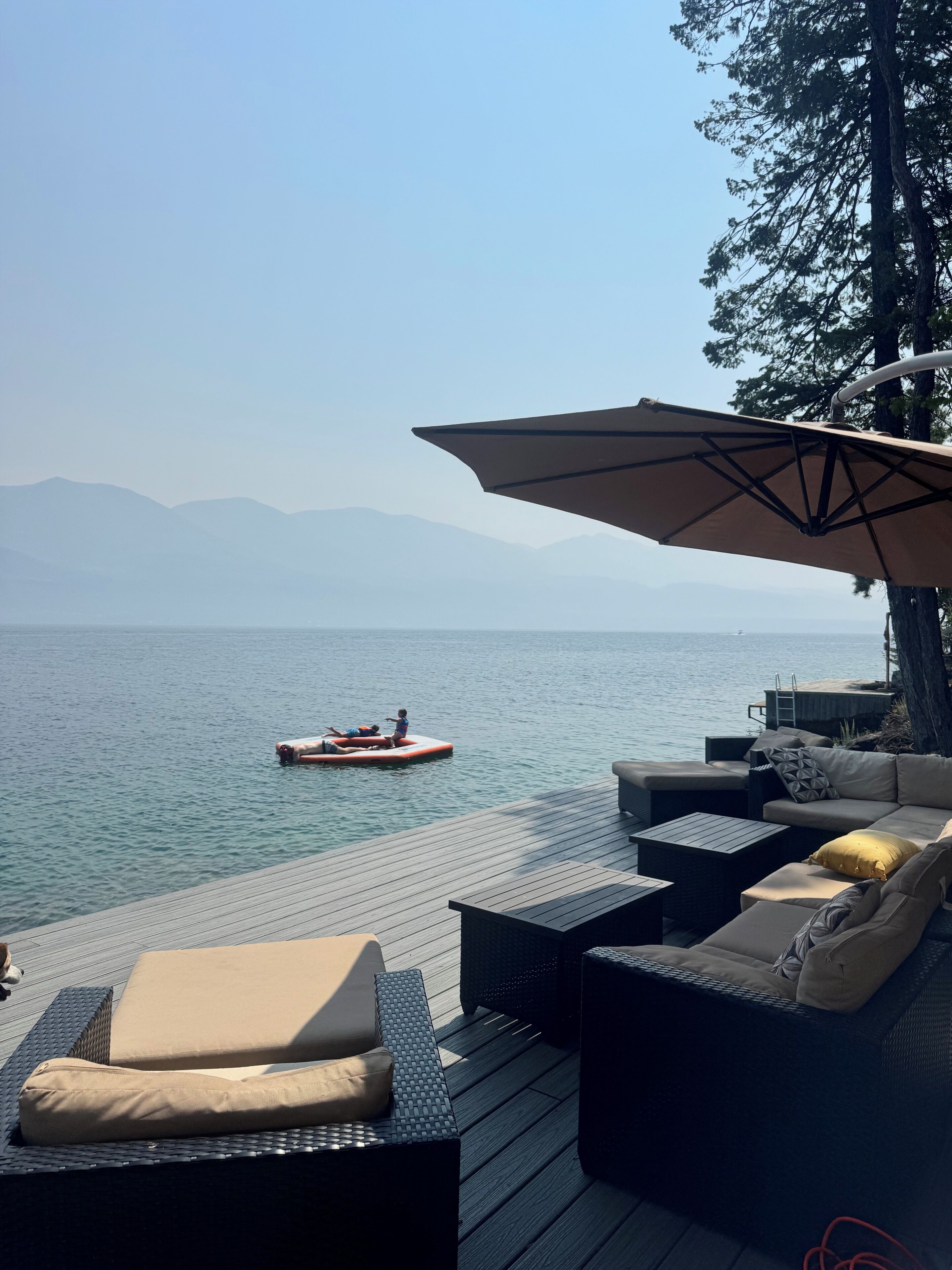 A deck with outdoor furniture overlooking a body of water and mountains.