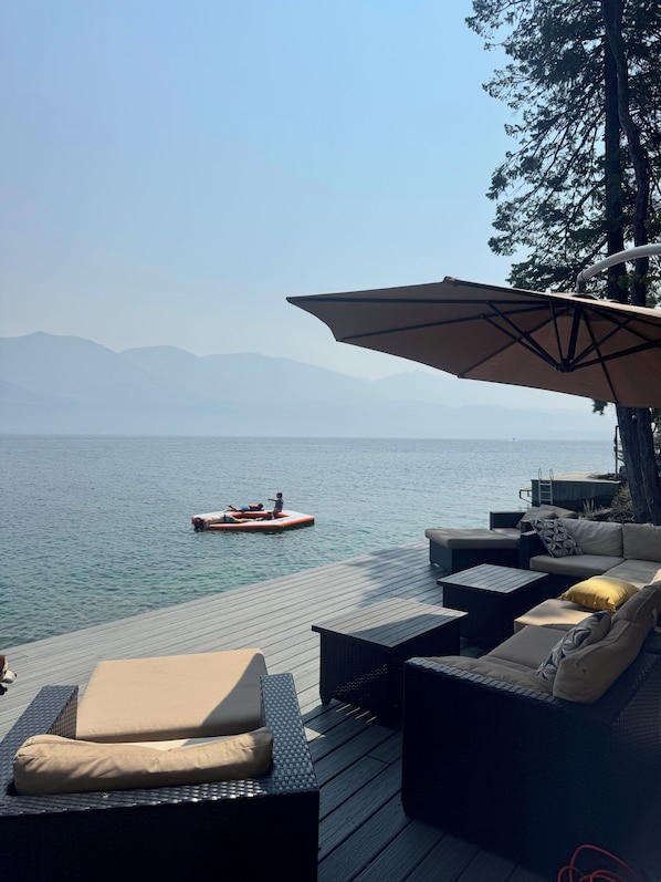 A deck with outdoor furniture overlooking a body of water and mountains.