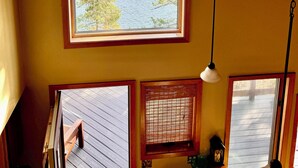 A room with a large arched window overlooking a body of water and trees, a wooden bench, and a hanging light fixture.