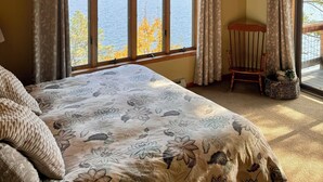 A bedroom with a large bed, a wooden ceiling, and a view of the sea through large windows.