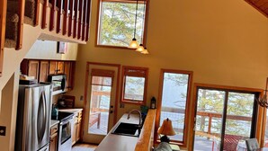 A spacious kitchen with a central island, wooden ceiling, and large windows offering views of the outdoors.