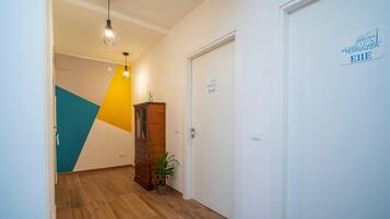 Un pasillo de hotel con piso de madera, diseño geométrico en la pared, un mueble de madera, una planta en maceta y una puerta con un letrero.