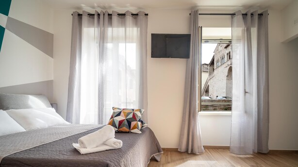 A modern hotel room with a large bed, a TV mounted on the wall, and a view of a building outside. - La Terrazza Anagni (Anagni)