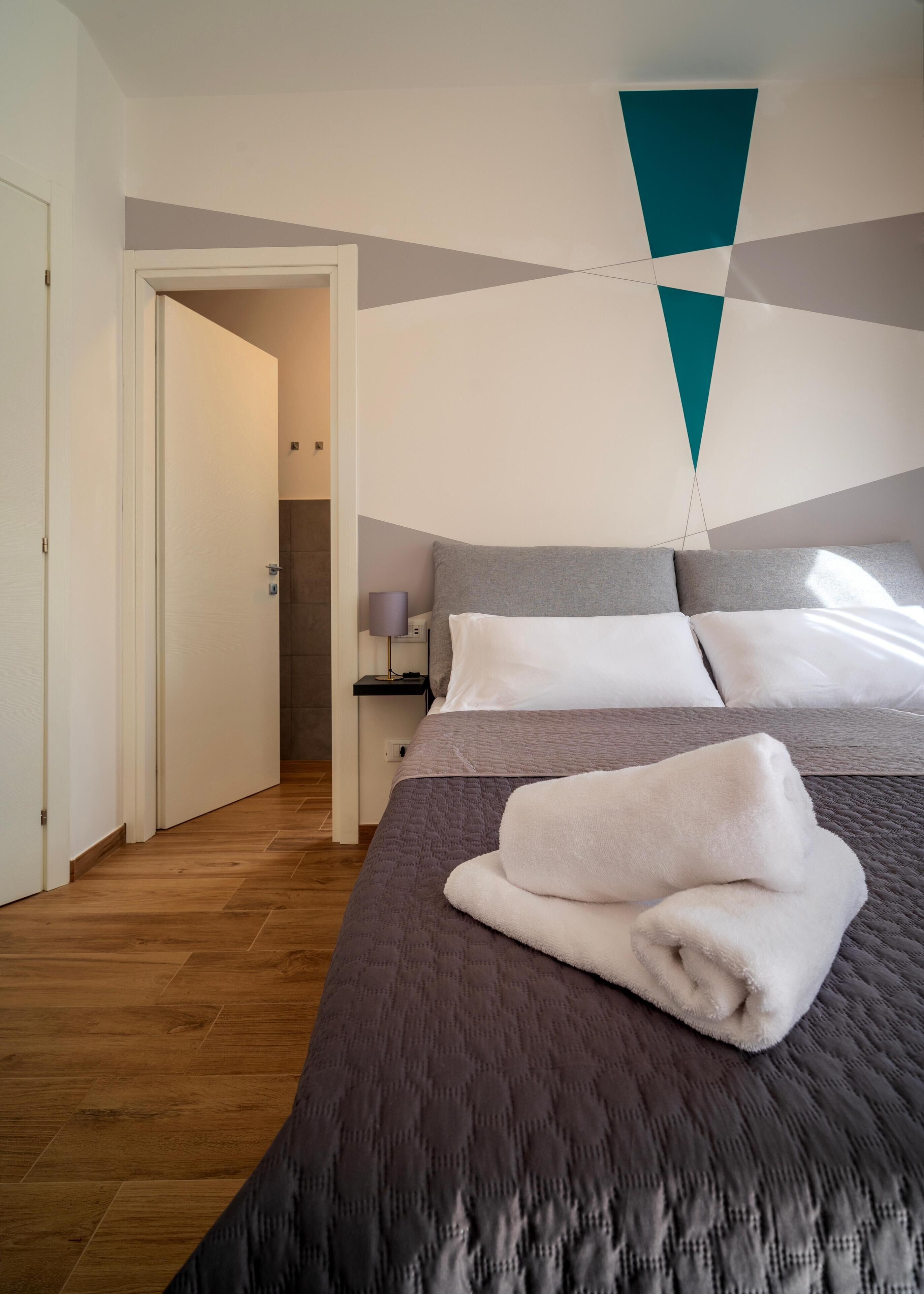 A modern hotel room with a large bed, a nightstand, and a geometric wall design.