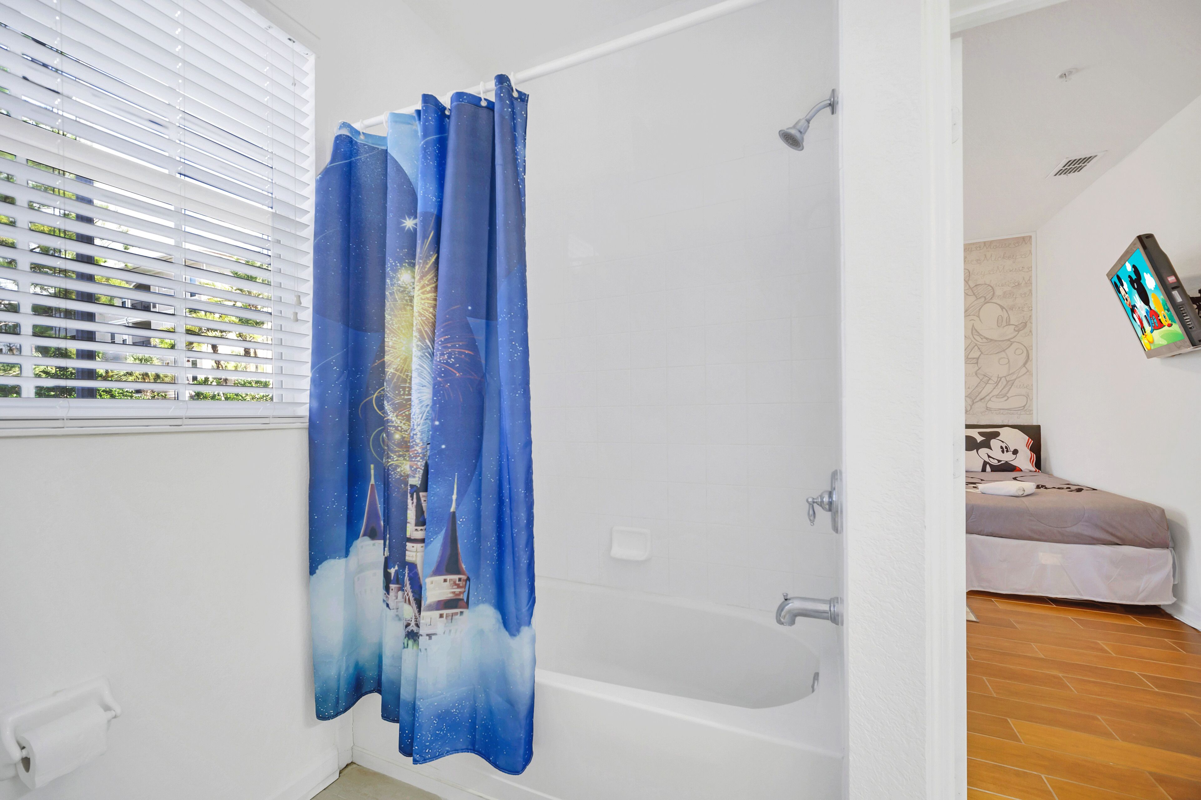 A bathroom with a shower curtain featuring a castle and fireworks, a toilet paper holder, and a showerhead.