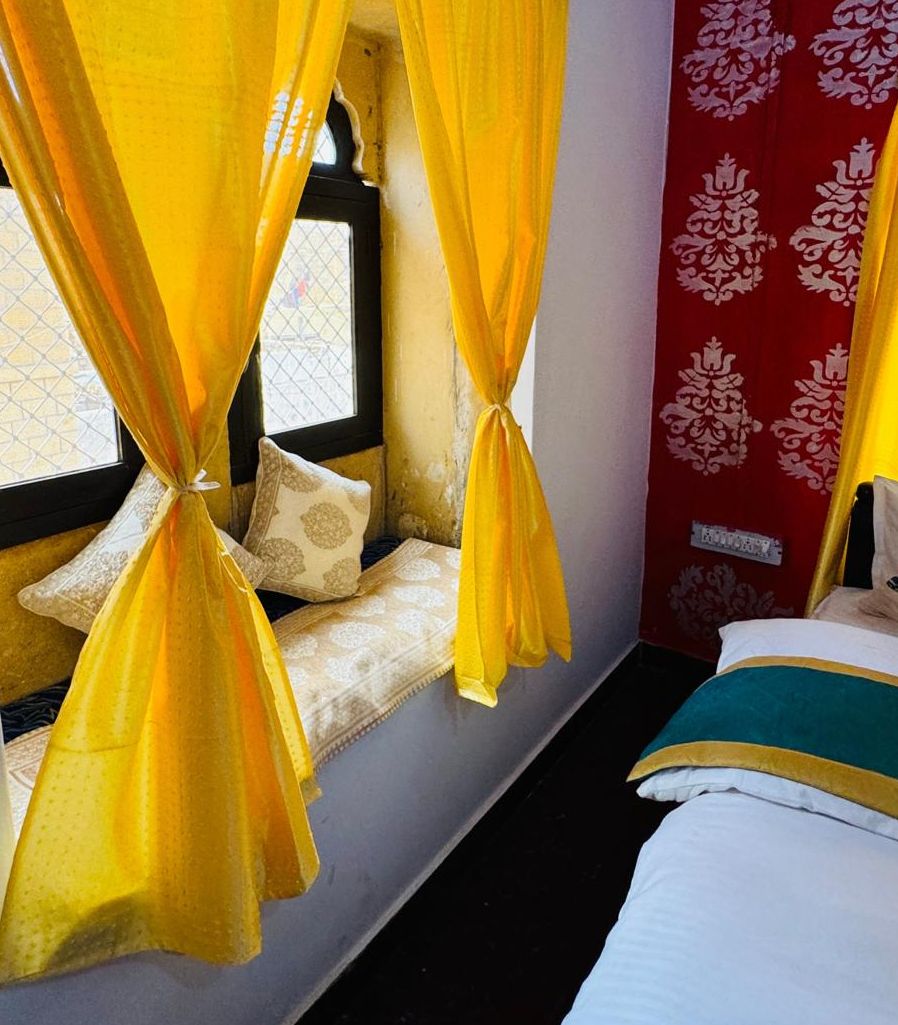 A room with a window, a bed, and yellow curtains tied at the top.