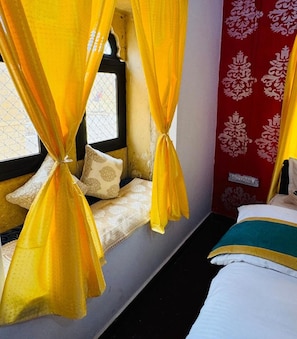 A room with a window, a bed, and yellow curtains tied at the top.
