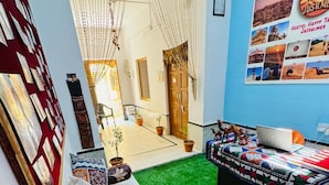 A room with a green artificial turf floor, a bed with a colorful quilt, a sofa with patterned cushions, and a wall decorated with a poster and framed pictures. - Happy Trails Jaisalmer (Jaisalmer)