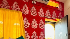 A room with a bed, a window with yellow curtains, and a red patterned wall. - Happy Trails Jaisalmer (Jaisalmer)