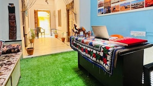 A room with a green artificial turf floor, a desk with a laptop, and a wall decorated with photos and a sign. - Happy Trails Jaisalmer (Jaisalmer)