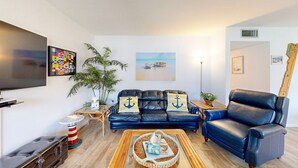 A living room with a black leather sofa, a coffee table, a television, and a large plant. - Beach Access Across the Street, Shared Heated Pool (Corpus Christi)