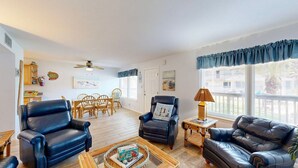 A spacious living room with leather sofas, a dining area with wicker furniture, and large windows with blue curtains. - Beach Access Across the Street, Shared Heated Pool (Corpus Christi)