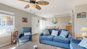 A living room with a blue sofa, a wooden coffee table, a ceiling fan, and a view of the outside. - Beach Access Across the Street, Shared Heated Pool (Corpus Christi)