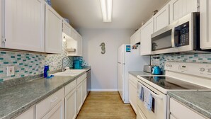 A narrow kitchen with white cabinets, a microwave, a stove, and a refrigerator. - Beach Access Across the Street, Shared Heated Pool (Corpus Christi)