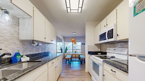 A modern kitchen with white cabinets, a granite countertop, a built-in oven, and a microwave.