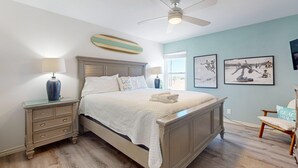 A bedroom with a bed, nightstands, a ceiling fan, and artwork on the walls.