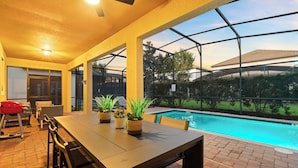 An outdoor pool area with a table and chairs, a ceiling fan, and potted plants.