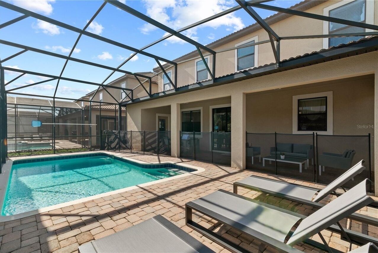 A pool area with lounge chairs, a glass-enclosed patio, and a view of a residential building.