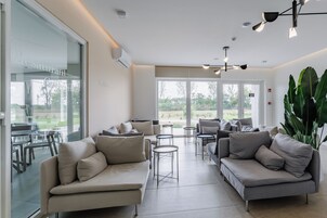 A modern interior with sofas, tables, and large windows offering a view of the outdoors.