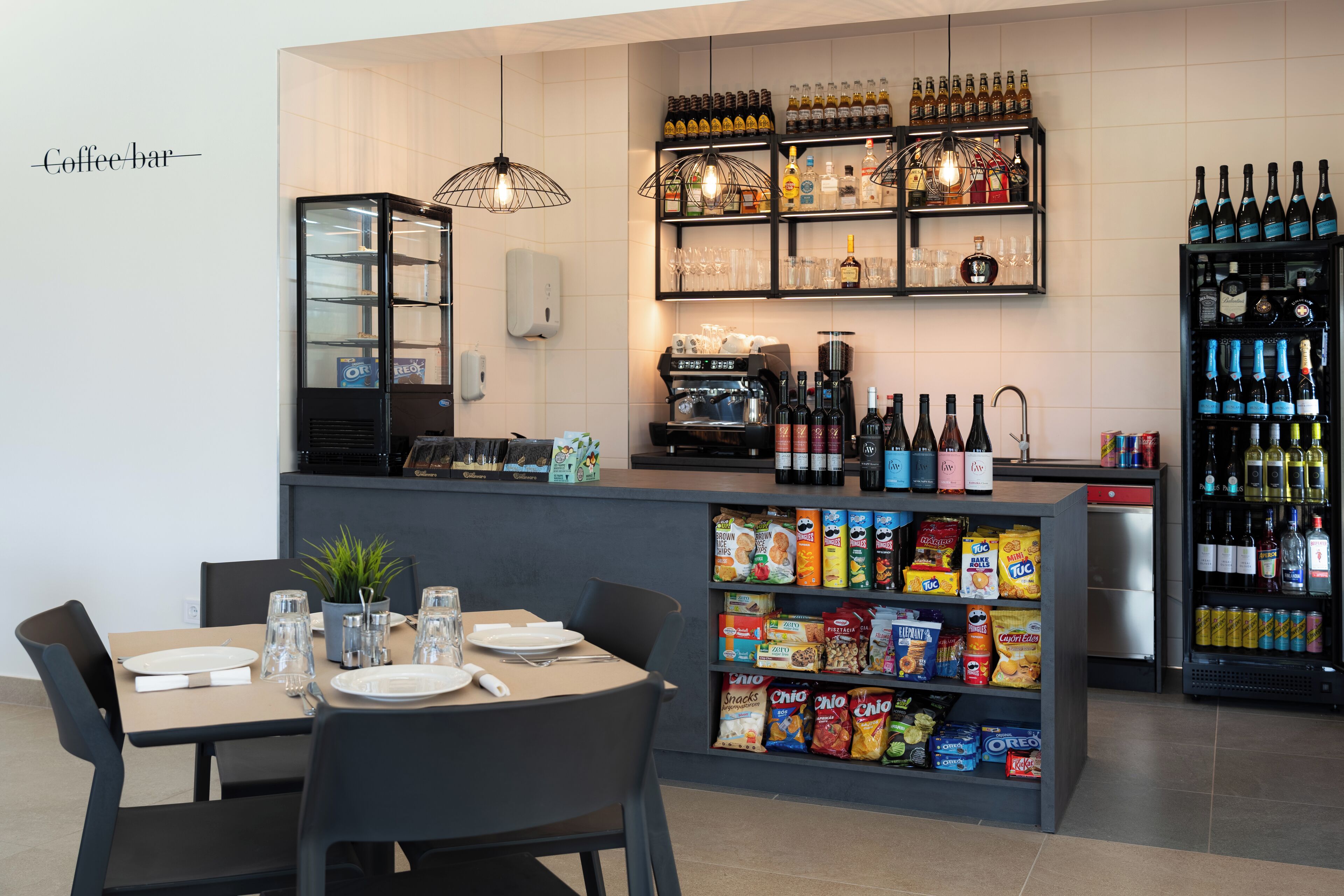 Un bar de café con estantes llenos de bebidas, una máquina de café y dispensadores de aperitivos.