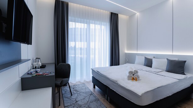 Una habitación de hotel moderna con una cama grande, un escritorio con televisor de pantalla plana y una zona de estar.