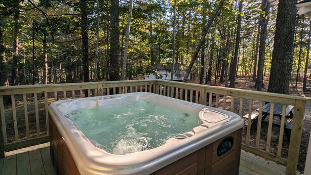 Un bain à remous sur une terrasse en bois, entouré d’arbres.
