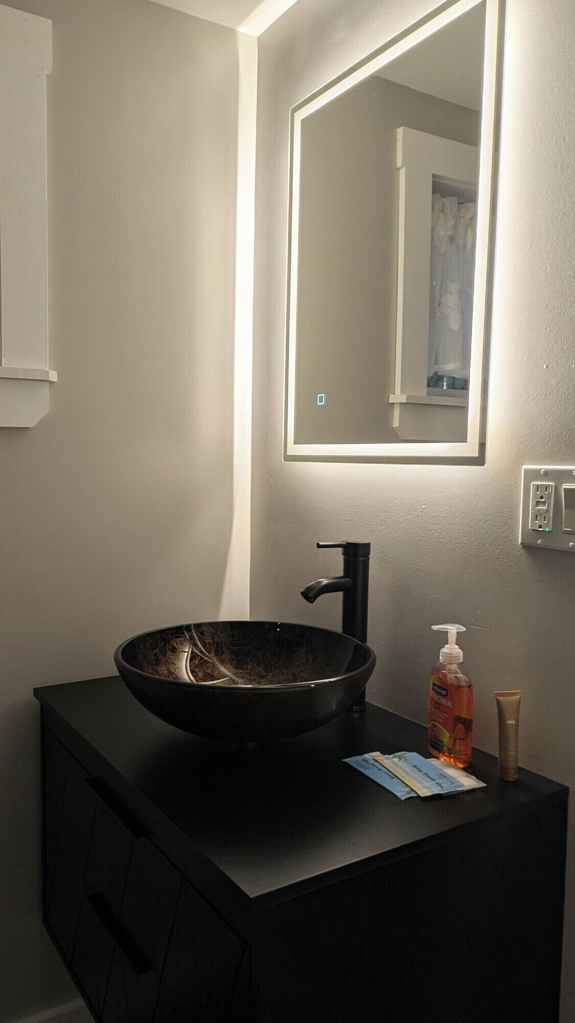 A bathroom with a black sink, a mirror, and toiletries on the counter.