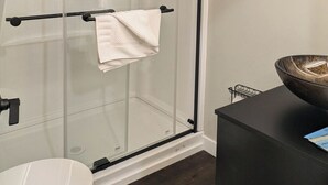 Une salle de bain moderne avec une douche à l’italienne en verre, des toilettes blanches et un meuble-lavabo noir.