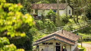 Ein kleines, eingeschossiges Haus mit Ziegeldach, umgeben von üppiger Vegetation und einem Holzzaun.