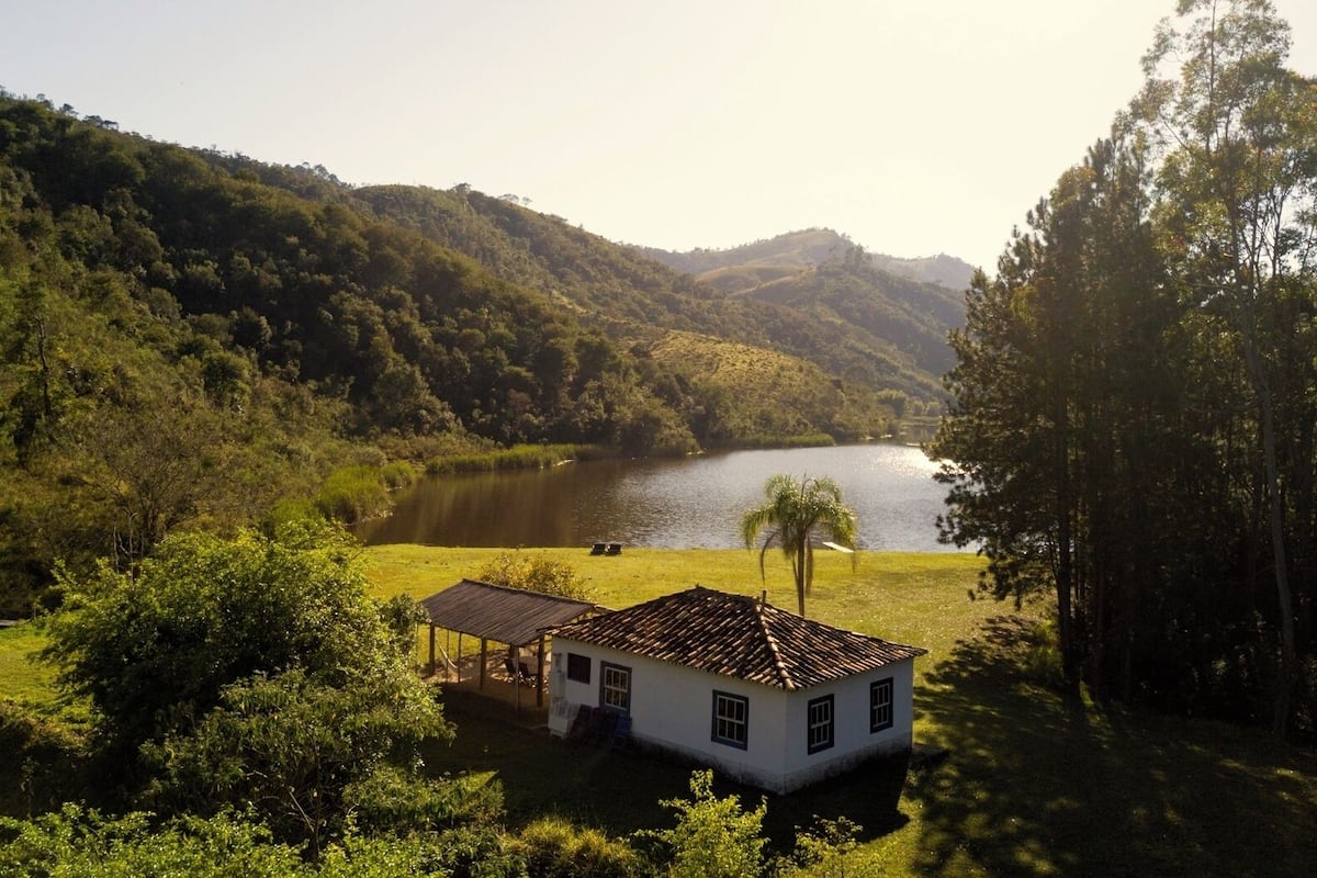 A house with a tiled roof, surrounded by lush greenery and a lake.