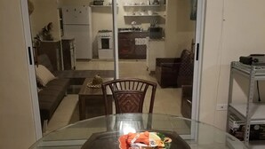 A dining area with a glass table surrounded by chairs, a bowl with snacks, and a view into a kitchen through a sliding door.