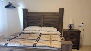 A bedroom with a wooden bed, a nightstand, a lamp, and an air conditioning unit on the wall.