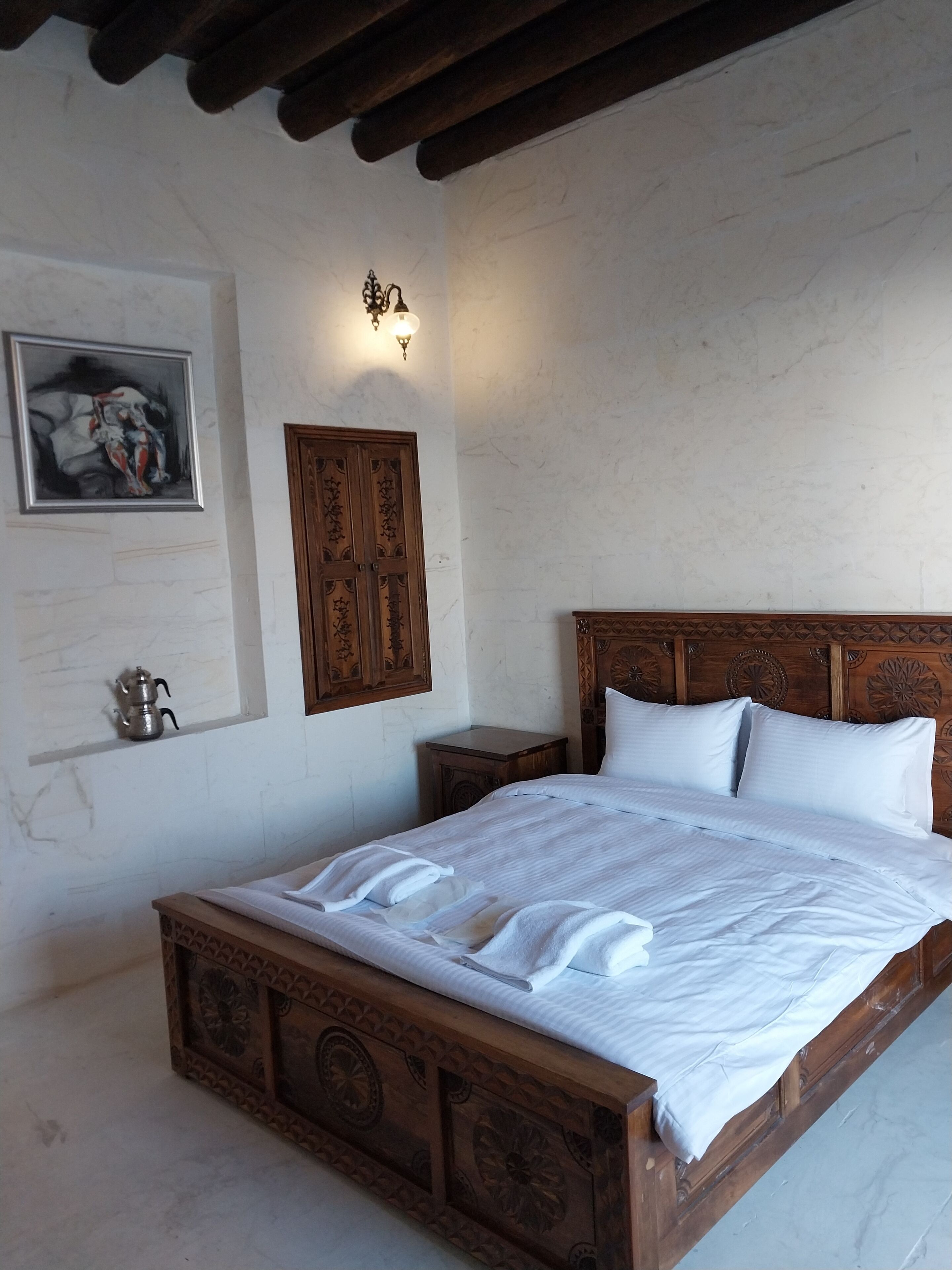 A neatly made bed with a wooden headboard, a small bedside table, and a wall-mounted light fixture.