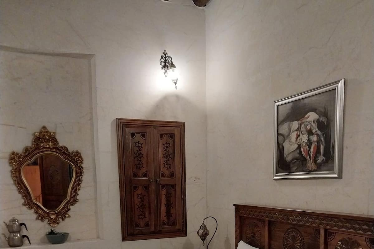 A neatly made bed with white linens and towels, a wooden headboard, a large mirror, a wooden wardrobe, and a framed painting on the wall.