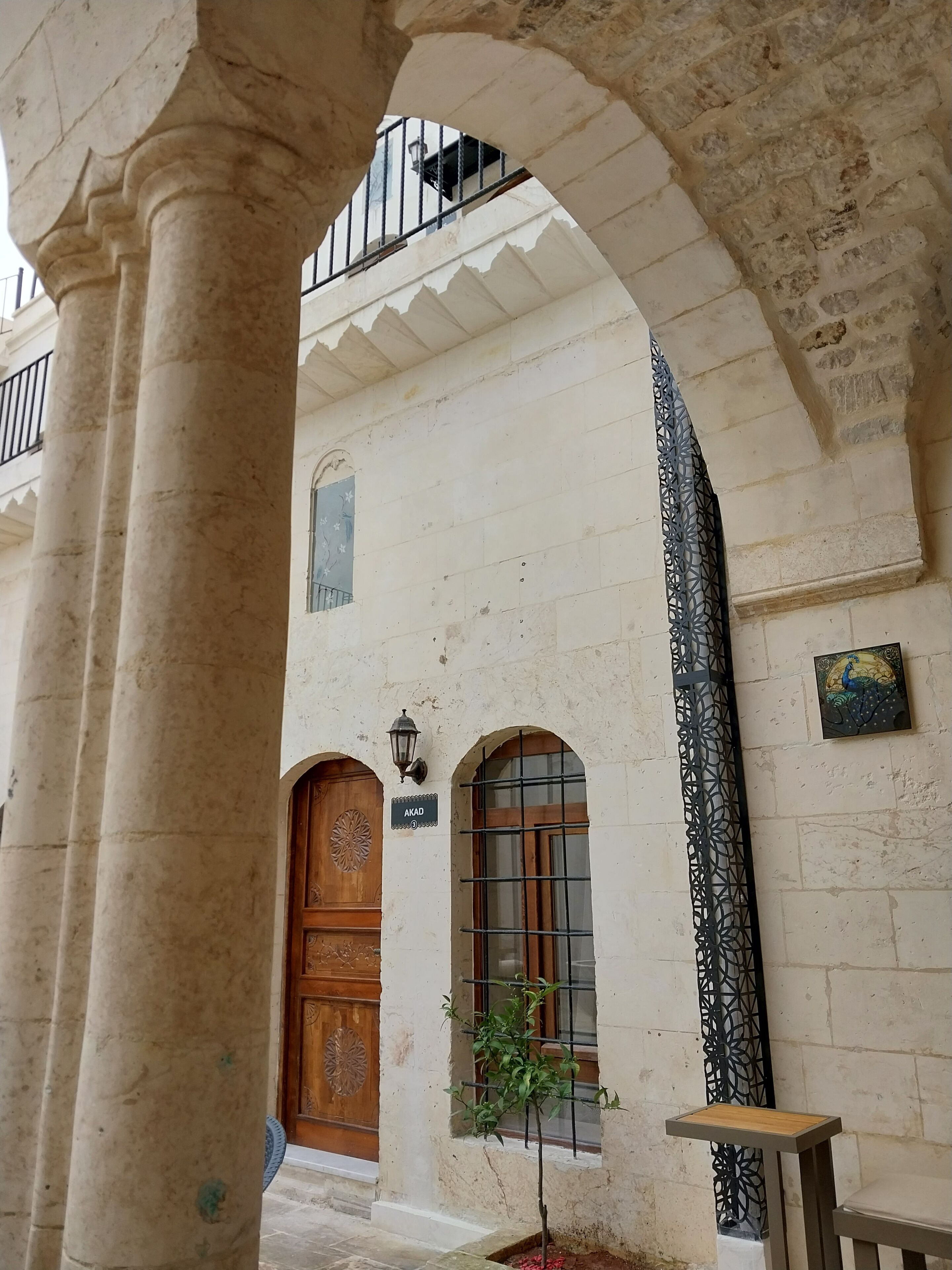 Un corridoio architettonico con una porta in legno, una piccola finestra con inferriata metallica e un pannello decorativo in metallo.