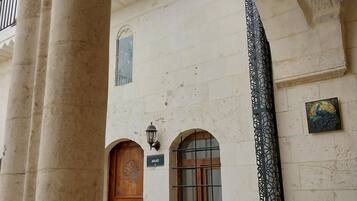 Un pasillo arquitectónico con una puerta de madera, una ventana pequeña con una reja metálica y un panel decorativo de metal.
