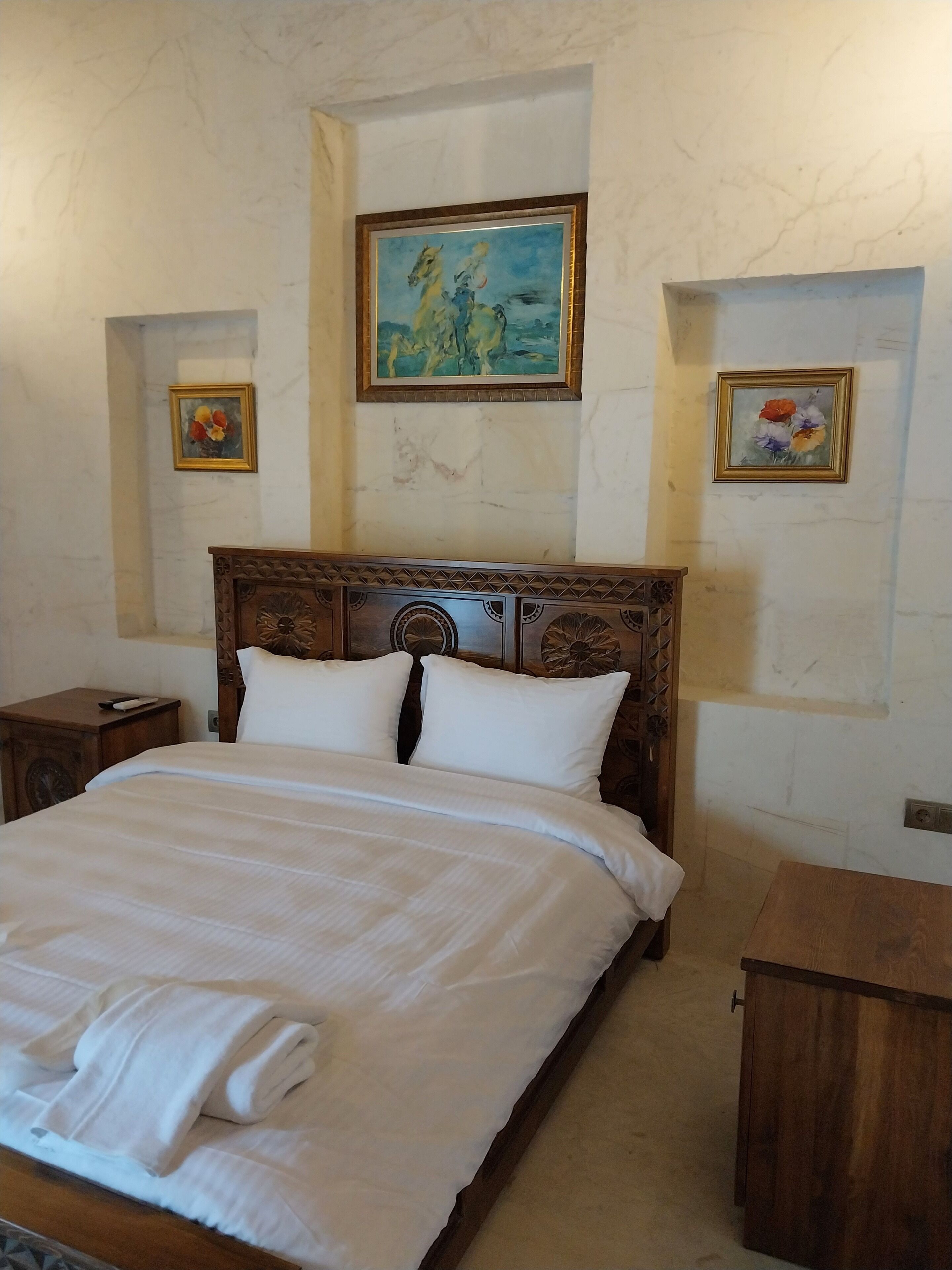 A neatly made bed with white linens and pillows, a wooden headboard, and a nightstand with a remote control.