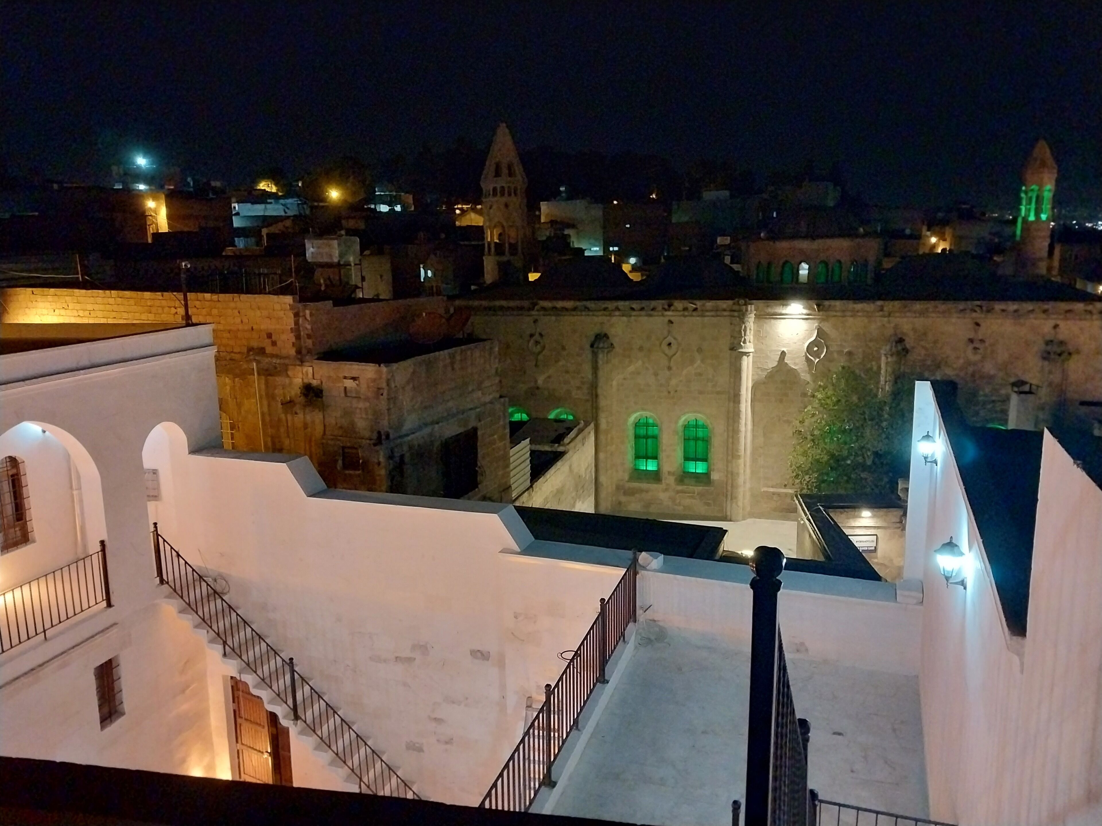 Una vista nocturna de un edificio histórico con una torre, ventanas en arco y una escalera que lleva a un nivel superior.