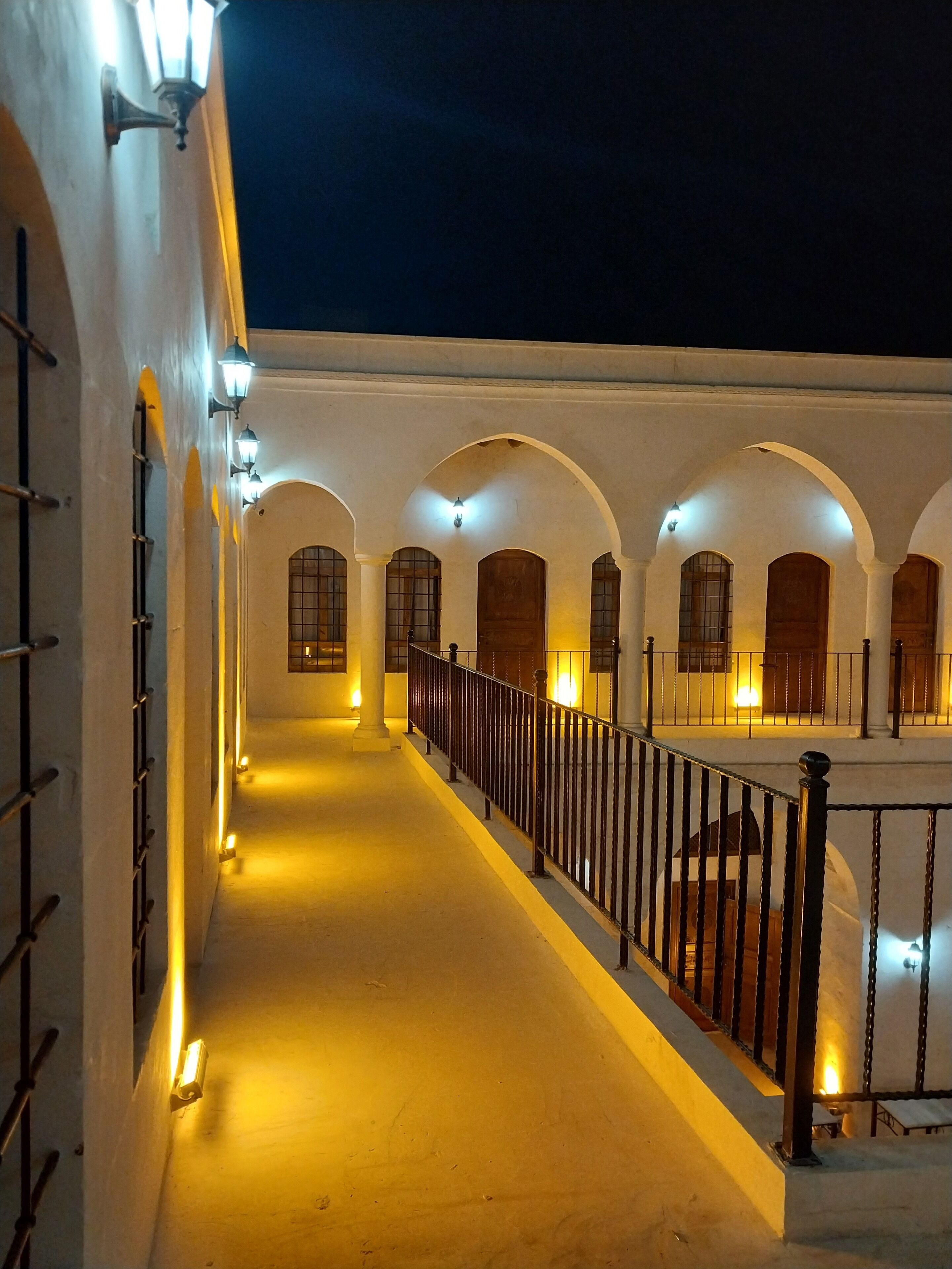 A well-lit corridor with arched doorways and a metal railing, suggesting a secure and inviting pathway within a building.